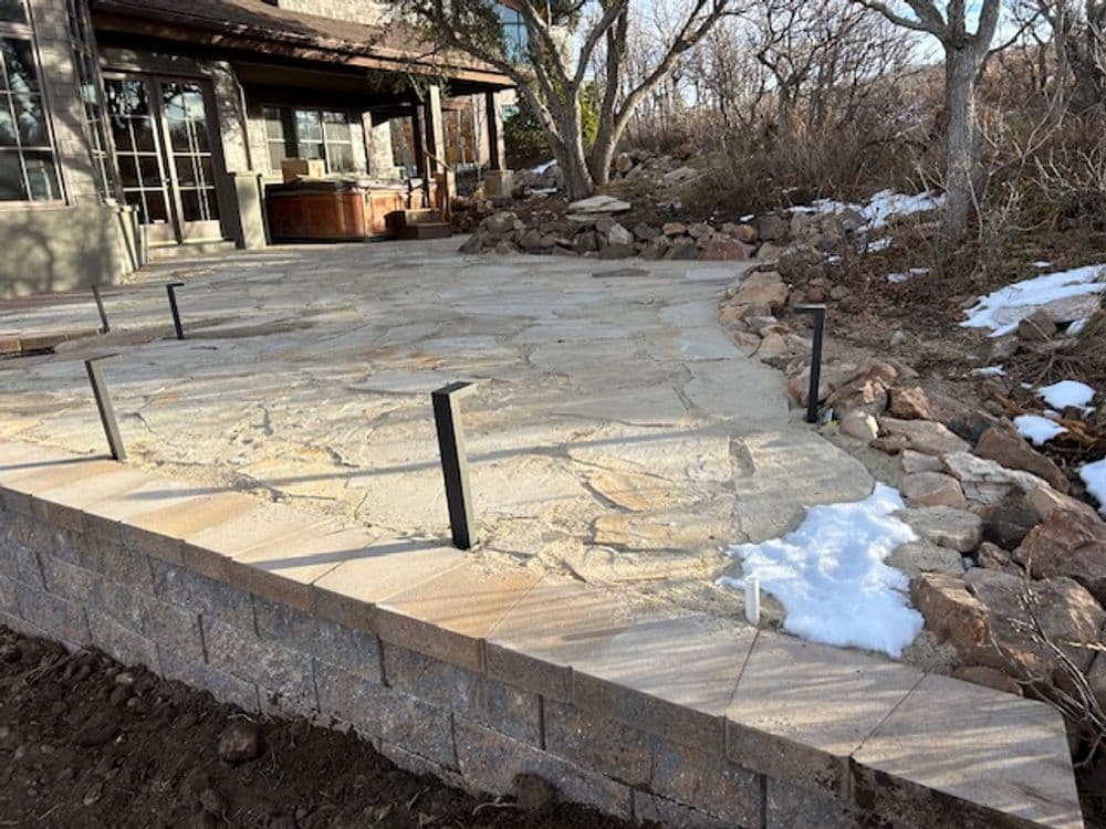 Stone patio area with a retaining wall, surrounded by trees and snow patches.