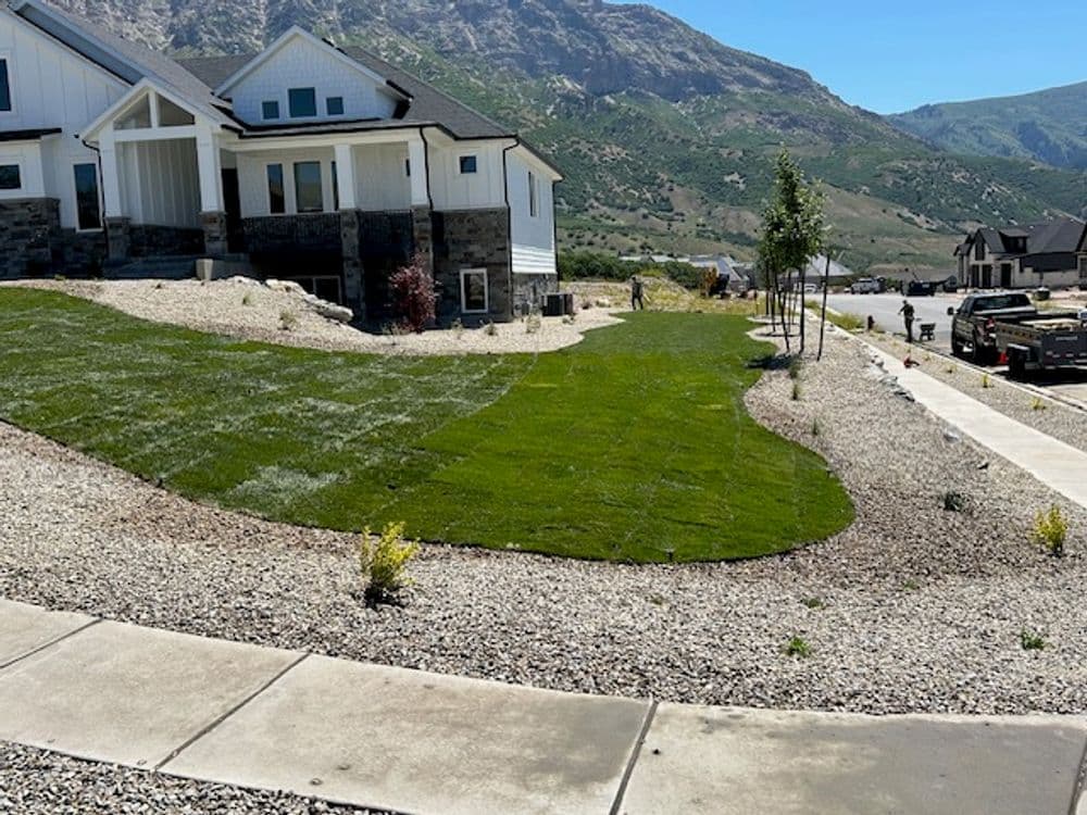 Newly landscaped home exterior with green lawn and gravel pathway, set against a mountain backdrop.