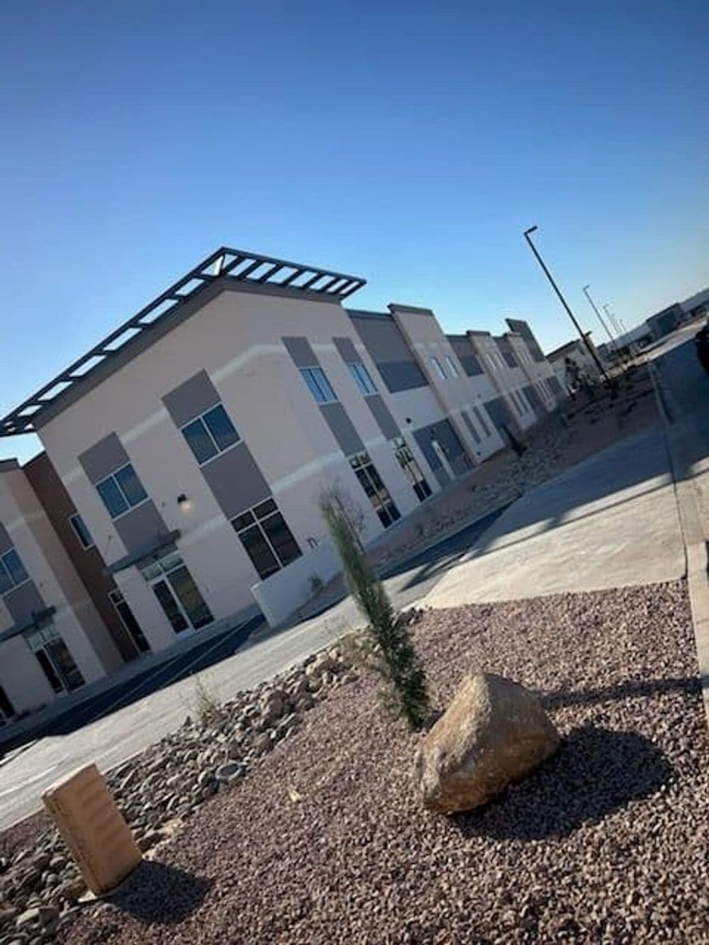 Modern commercial building with a landscaped pathway and desert plants under a clear blue sky.