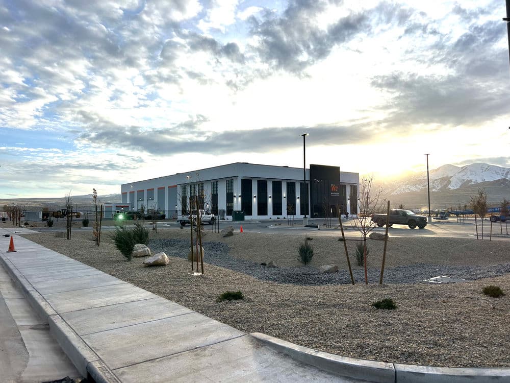 Modern commercial building with landscaping, mountains, and a cloudy sky at sunset.
