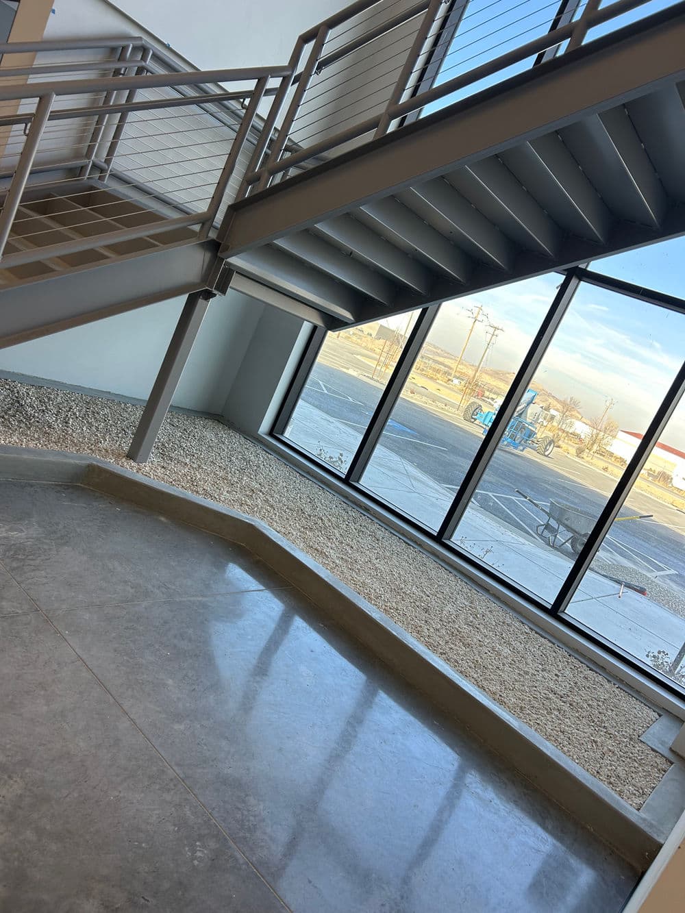Modern interior with staircase and large window overlooking gravel area and street.