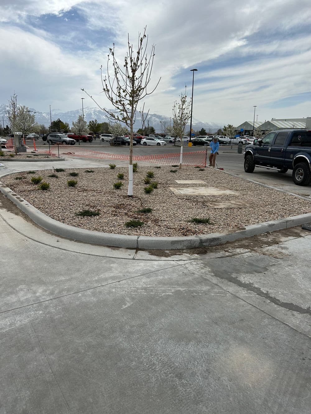 Parking lot landscape featuring newly planted trees, gravel, and construction activities nearby.