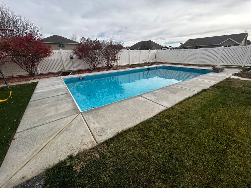 Backyard swimming pool surrounded by grass and landscaped gardens under a cloudy sky.