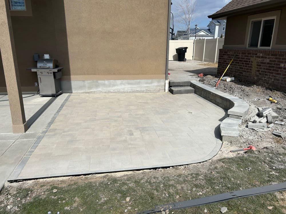 Paved patio area with gray stone, adjacent to a house and a grill, under construction.