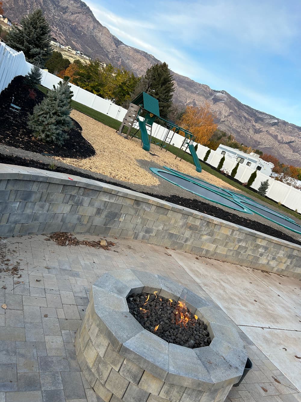 Fire pit surrounded by stone patio, playground, and mountains in the background.
