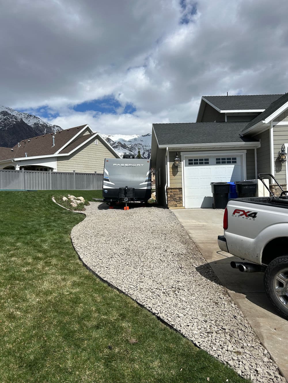 RV parked beside a house with mountains in the background and a gravel driveway.