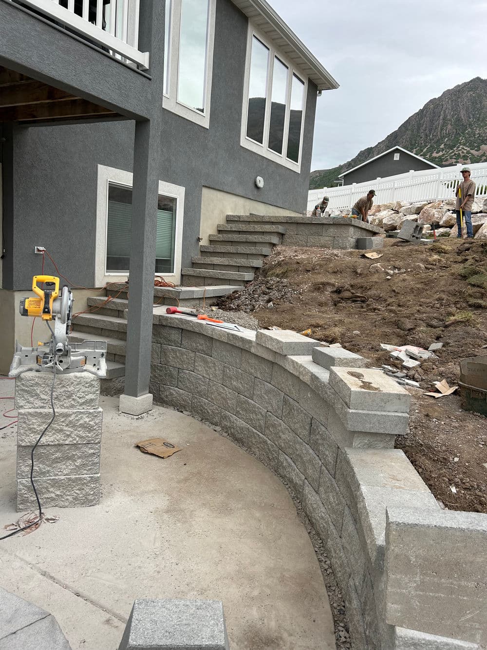 Construction of retaining wall and landscaping near modern home with mountain backdrop.