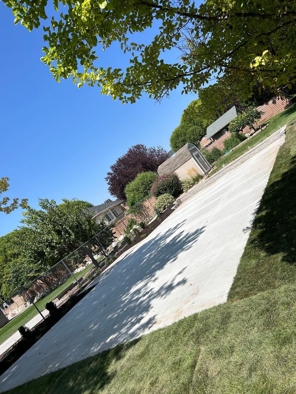 Clear view of a landscaped yard with a freshly poured concrete area and residential buildings.