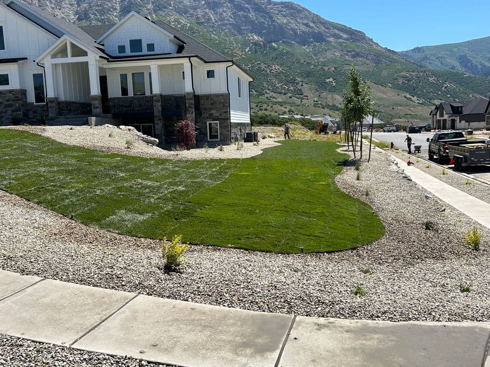 Newly landscaped home exterior with green lawn, gravel, and mountain backdrop.