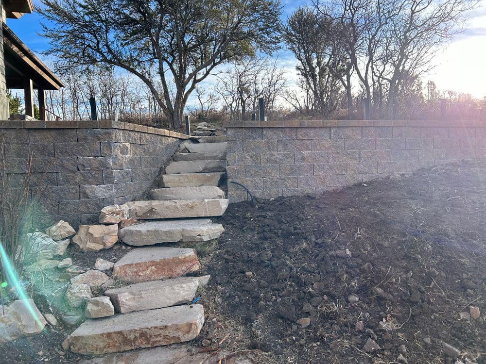 Stone steps leading up to a landscaped area with trees and a stone wall.