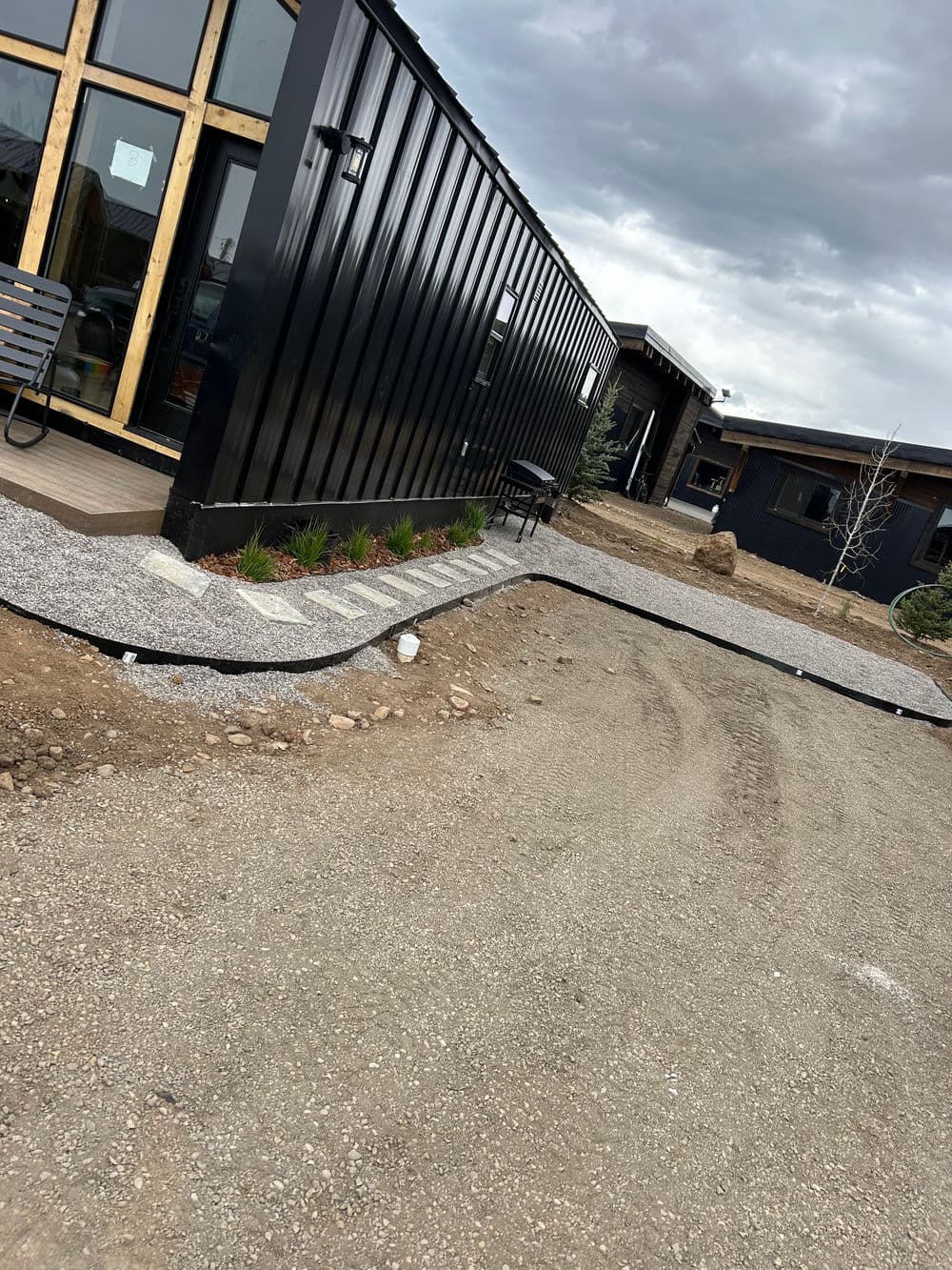 Modern black building with gravel pathway and landscaping in foreground under cloudy sky.