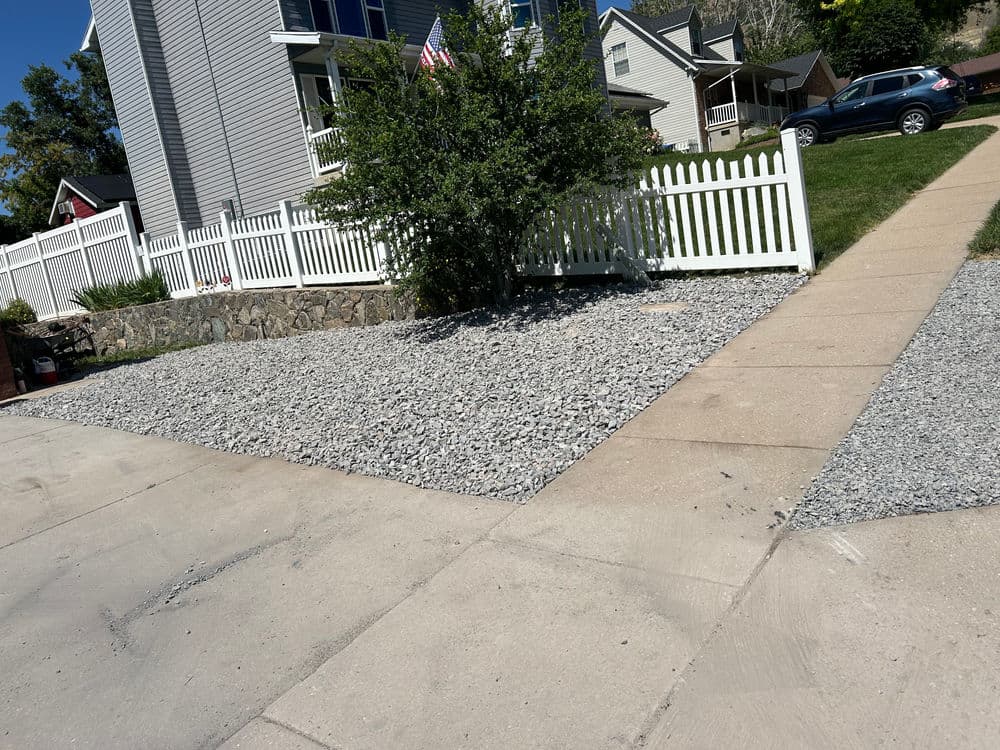 Gravel landscape with white picket fence and concrete walkway outside residential home.