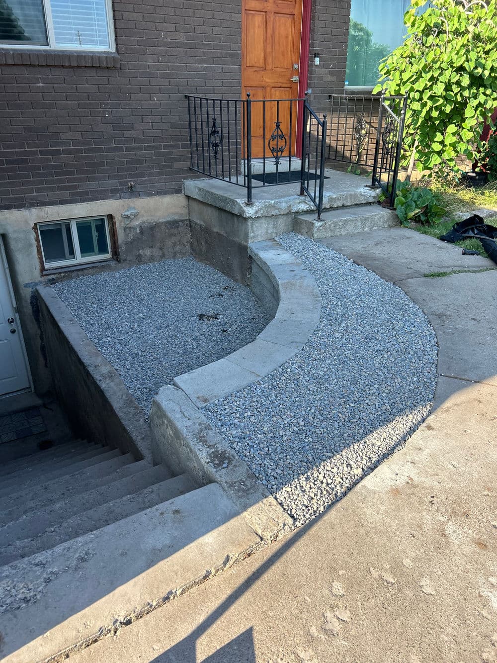 Curved gravel pathway leading to a brown door and stairs with black railing.
