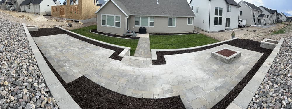 Panoramic view of a newly landscaped backyard with stone pathways and house in background.