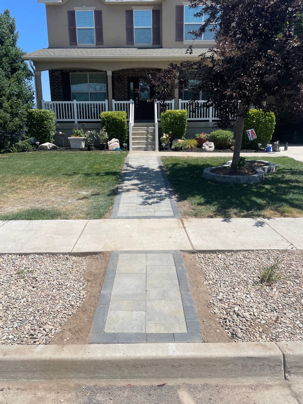 Sidewalk leading to a cozy home with shrubs and a landscaped yard.