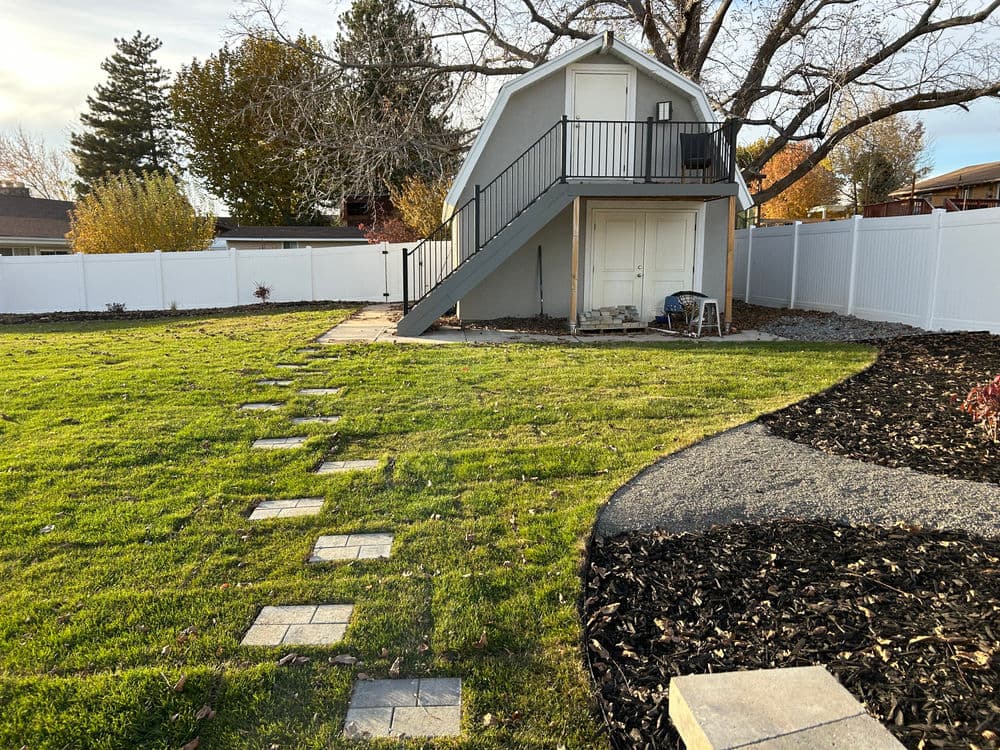 Two-story backyard shed with stairs surrounded by lawn and landscaped path.