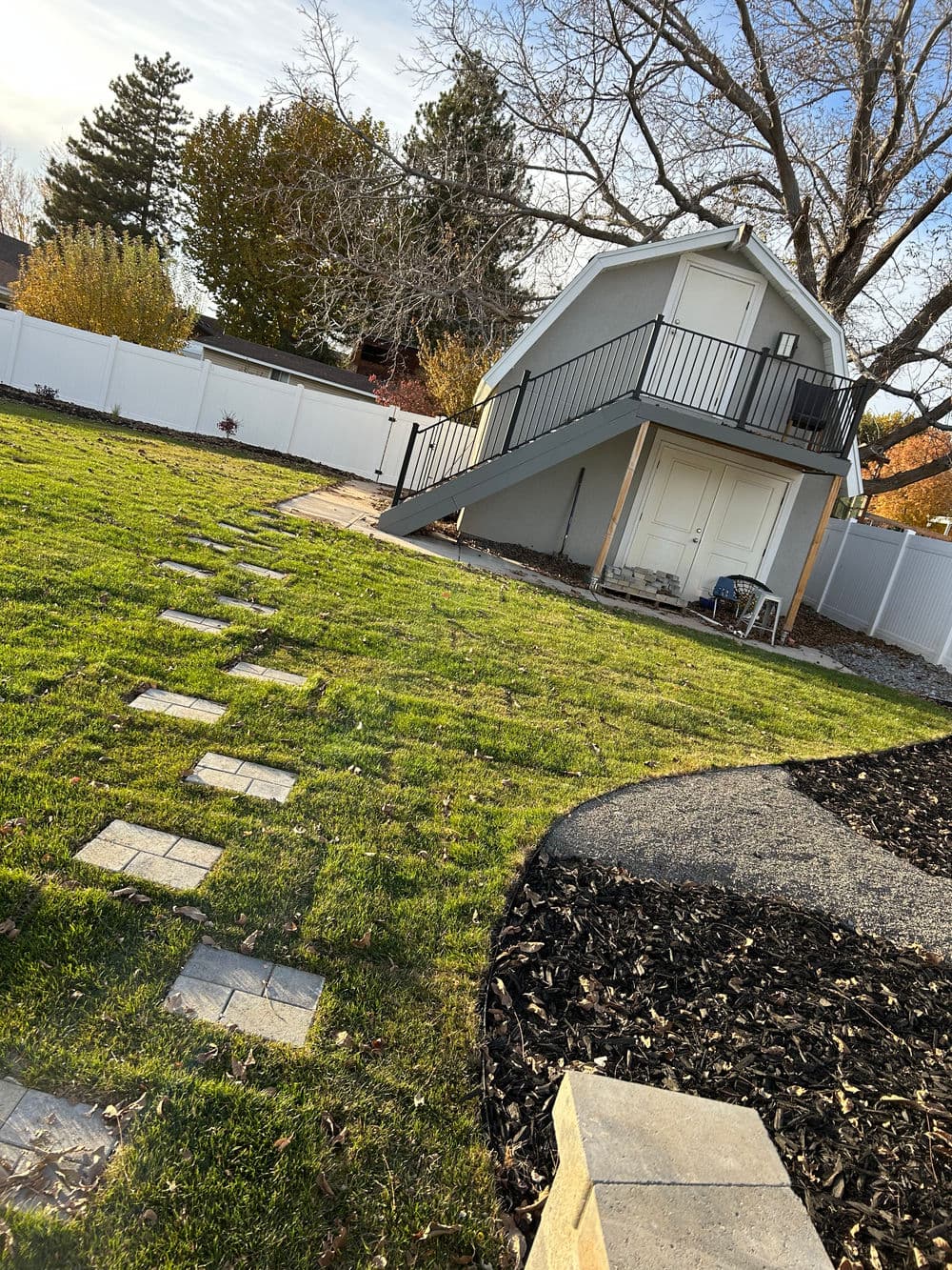Backyard with a modern shed, grass lawn, stone pathway, and white fencing.