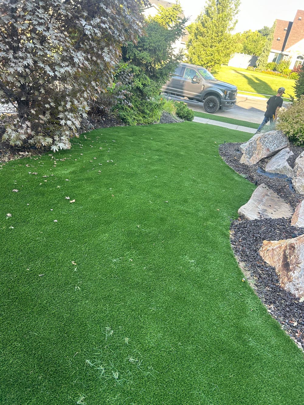 Lush green artificial lawn with rocks and a parked truck in a residential area.